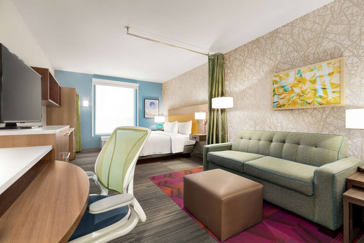 Une chambre d’hôtel avec un lit, un canapé vert, un bureau avec un ordinateur, une chaise et un téléviseur.