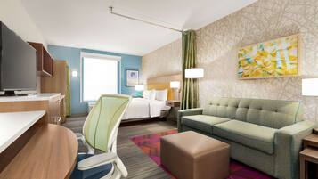 A hotel room with a bed, a green sofa, a desk with a computer, a chair, and a TV.