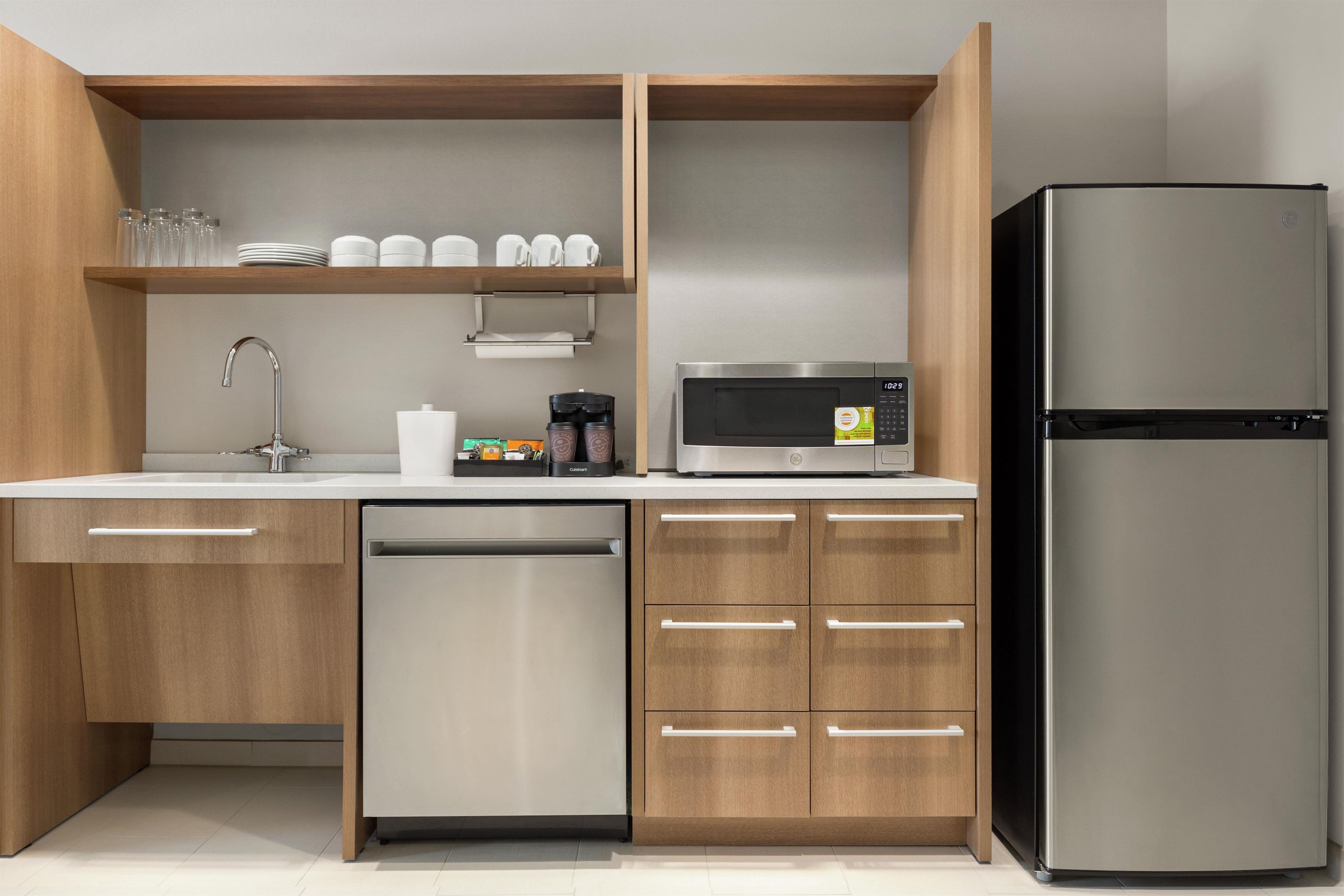 A modern kitchen with wooden cabinets, a stainless steel dishwasher, a black refrigerator, a microwave, and a coffee maker.