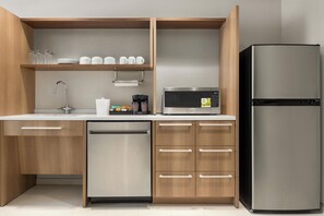 Une cuisine moderne avec des meubles en bois, un lave-vaisselle en acier inoxydable, un réfrigérateur noir, un four à micro-ondes et une machine à café.
