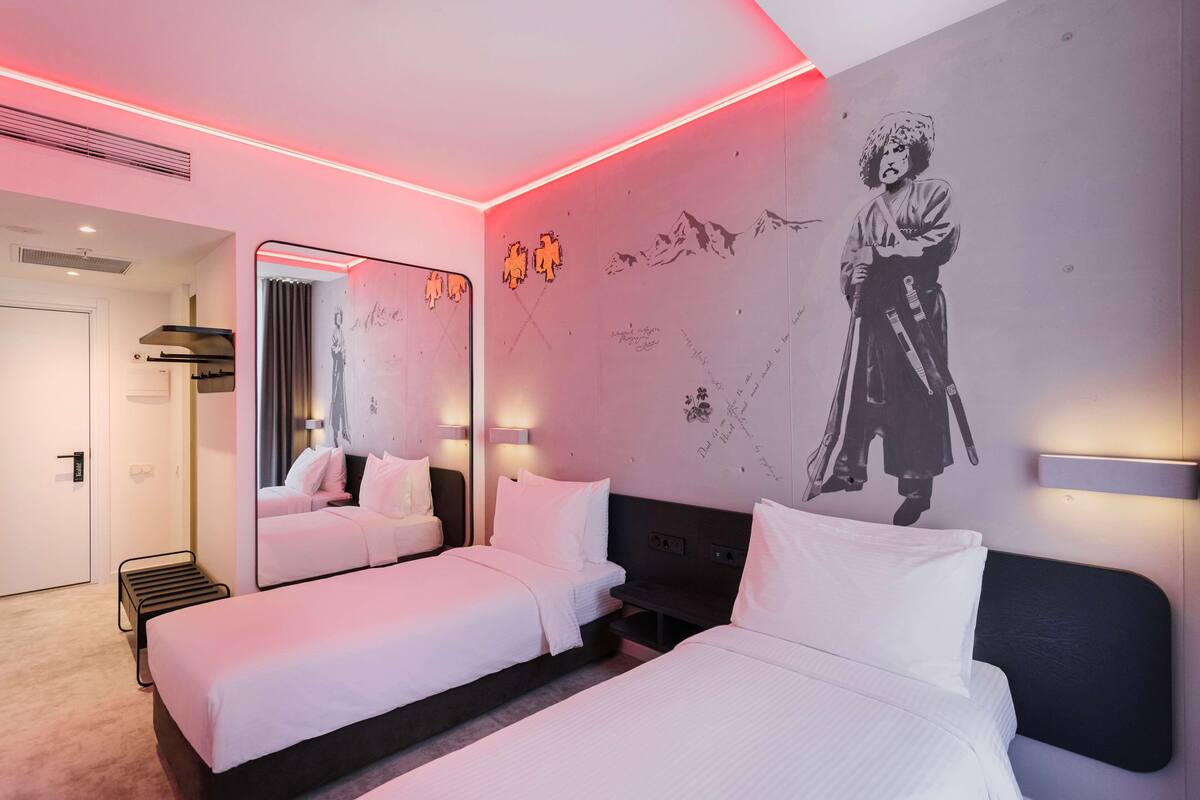 A hotel room with two beds, a large mirror, and a wall with a mural.