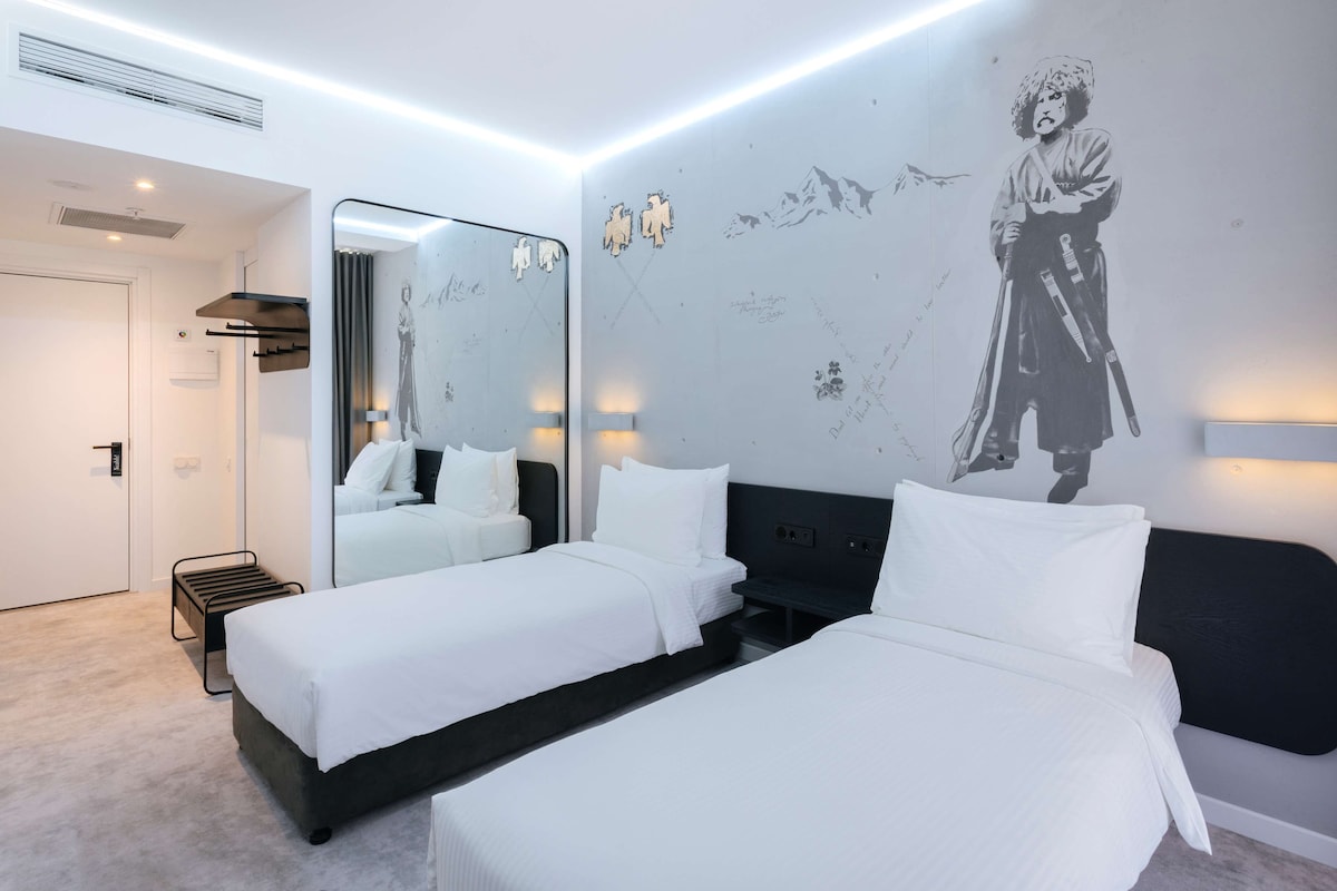 Une chambre d’hôtel moderne avec deux lits, un grand miroir et une fresque murale.