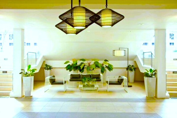 A spacious lobby with a central seating area, potted plants, and a staircase.