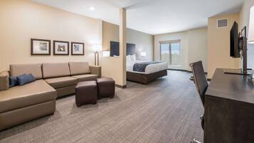 A hotel room with a large sofa, a bed, a desk, and a television.