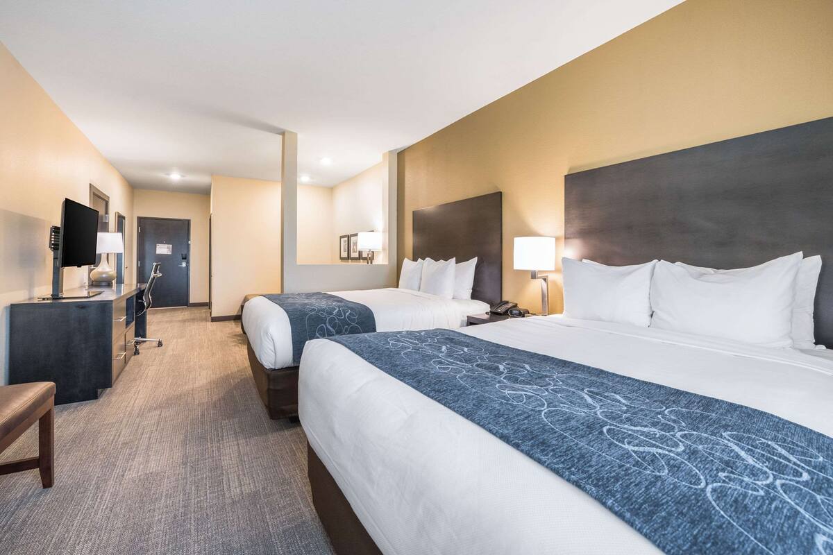 A hotel room with two beds, a desk, a chair, and a television.