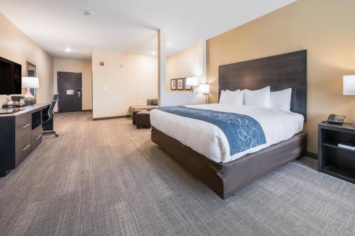 A hotel room with a large bed, a desk, a chair, and a small table.
