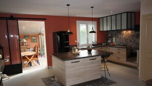 A modern kitchen with a central island, pendant lighting, and a view into the dining area.
