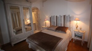 A bedroom with a large bed, a wardrobe, two bedside tables with lamps, and a mirror.