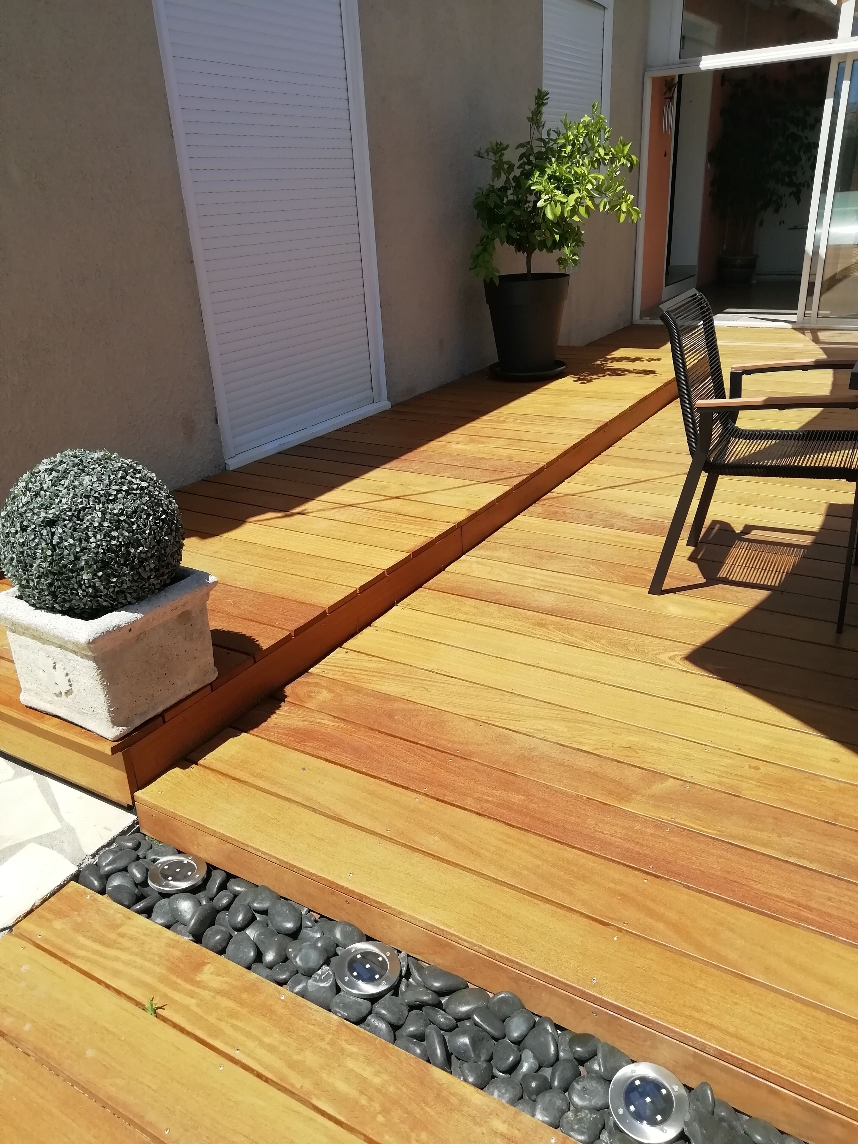 Eine Holzterrasse mit einem Pflanzgefäß, einer Topfpflanze und einem Stuhl.