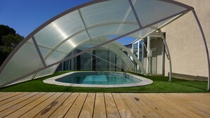 A swimming pool under a transparent canopy, surrounded by artificial grass and wooden decking.