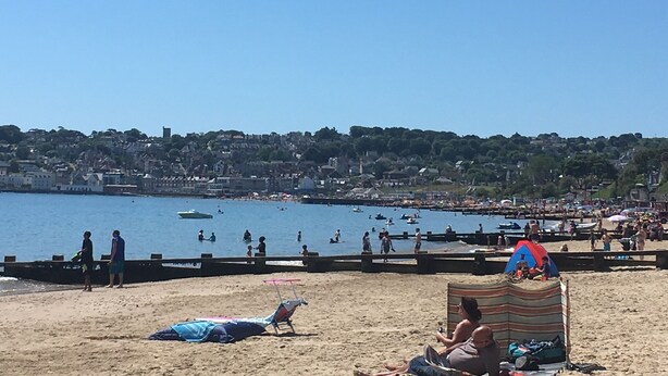 Une plage avec des gens, une jetée et un paysage urbain en arrière-plan.