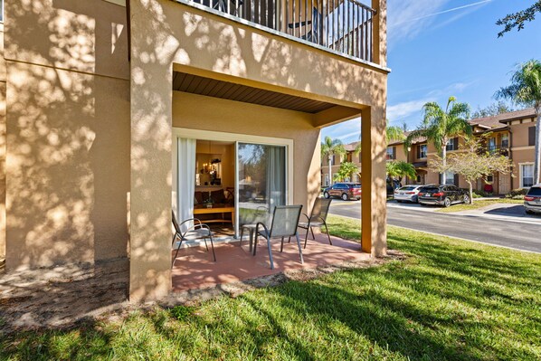 A building with a covered outdoor seating area, a balcony, and a view of a street with parked cars and palm trees. - Charming and Comfy Townhouse at Regal Palms Resort, just 15 minutes from Disney (Davenport)