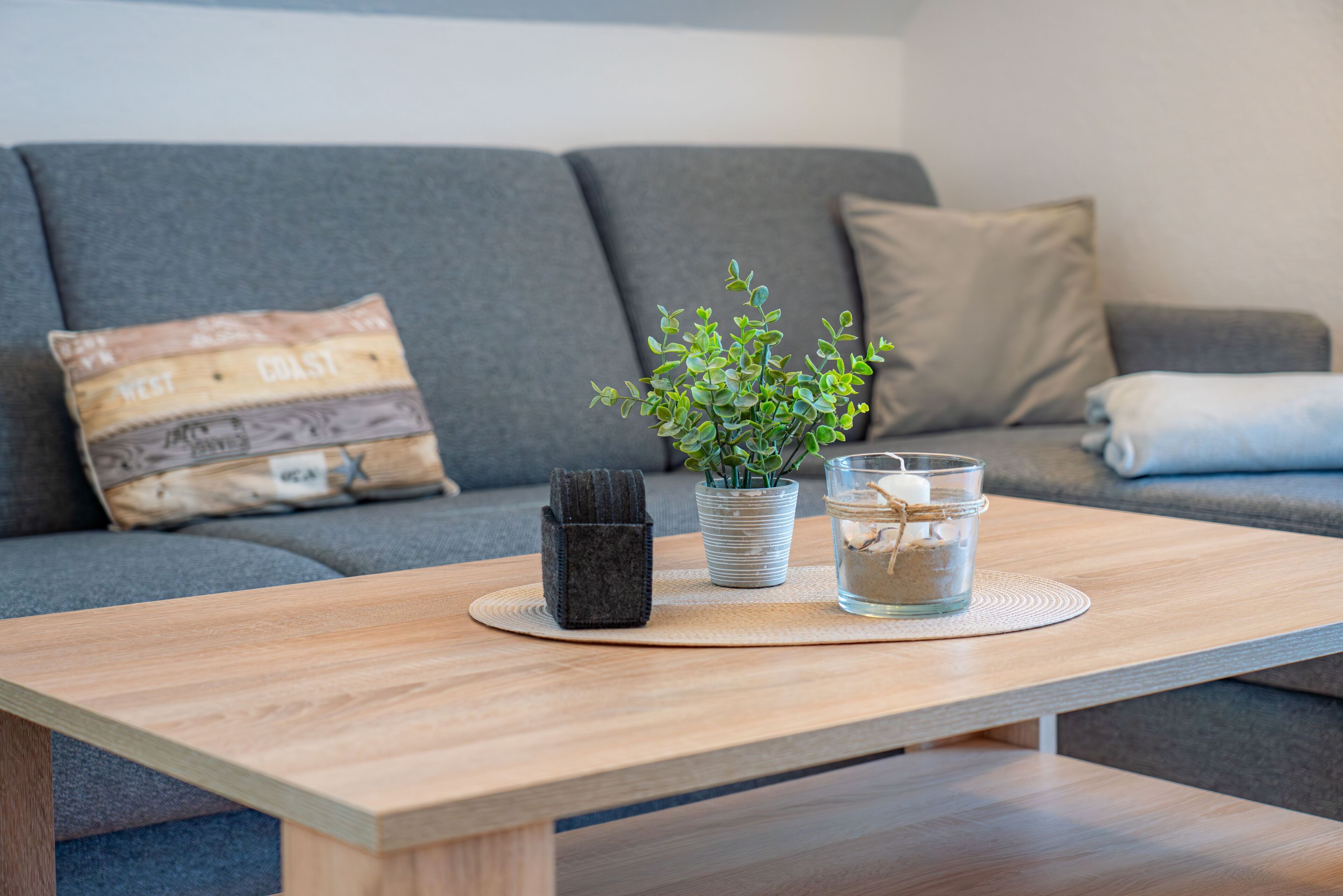 A wooden table with a potted plant, a glass container, and a small black bag on a woven placemat.