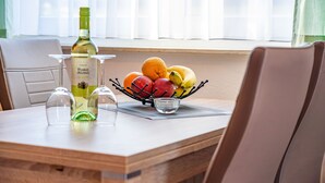 A dining table with a fruit bowl, a bottle of Muskat Ottonel wine, and two wine glasses. - Hus Günter - Apartment Maritim (Seebad Ahlbeck)