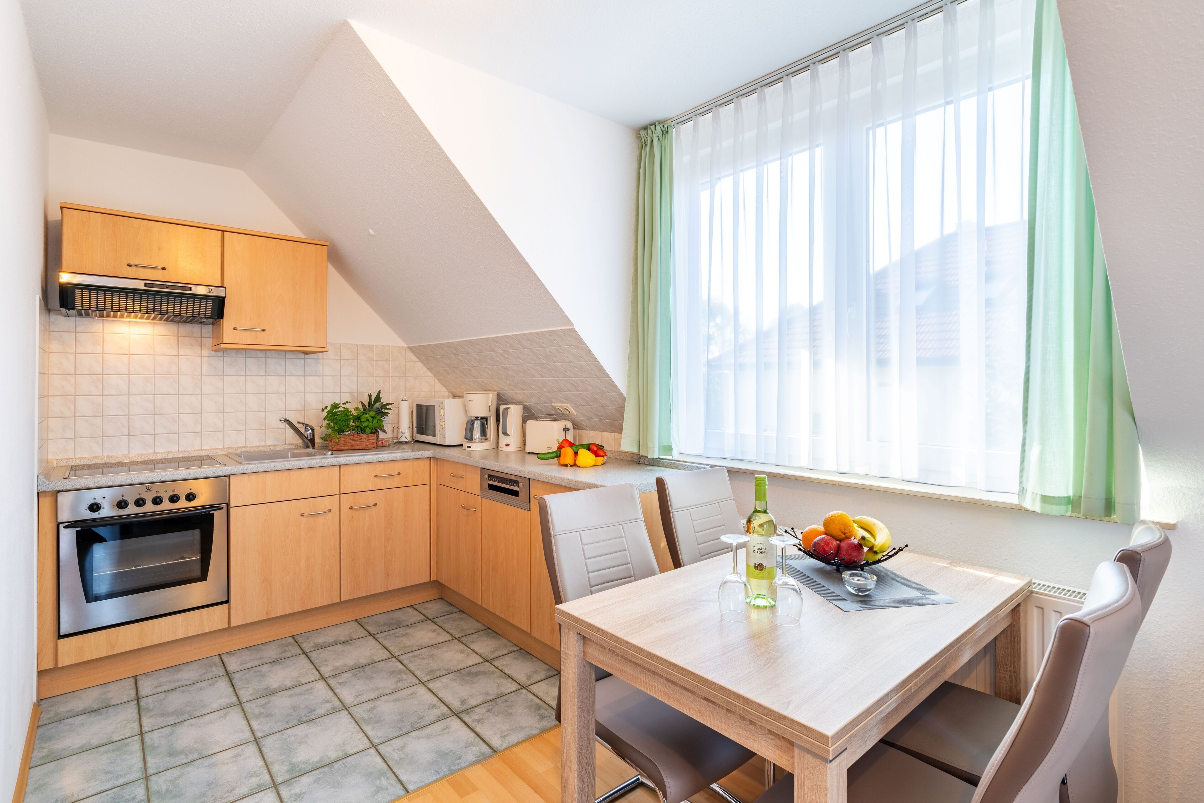 A modern kitchen with a dining area, featuring a built-in oven, microwave, and a window with sheer curtains.