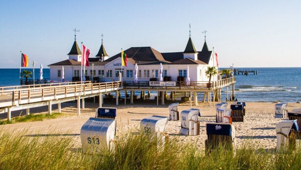 A beachfront hotel with a pier, beachside seating, and flags. - Hus Günter - Apartment Nautilus (Seebad Ahlbeck)
