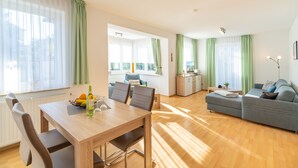 A spacious living area with a dining table, sofa, and kitchen in the background. - Hus Günter - Apartment Nautilus (Seebad Ahlbeck)