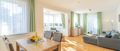 A spacious living area with a dining table, sofa, and kitchen in the background.