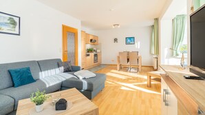 A modern living room with a grey sofa, a wooden coffee table, and a TV on a wooden stand. - Hus Günter - Apartment Nautilus (Seebad Ahlbeck)