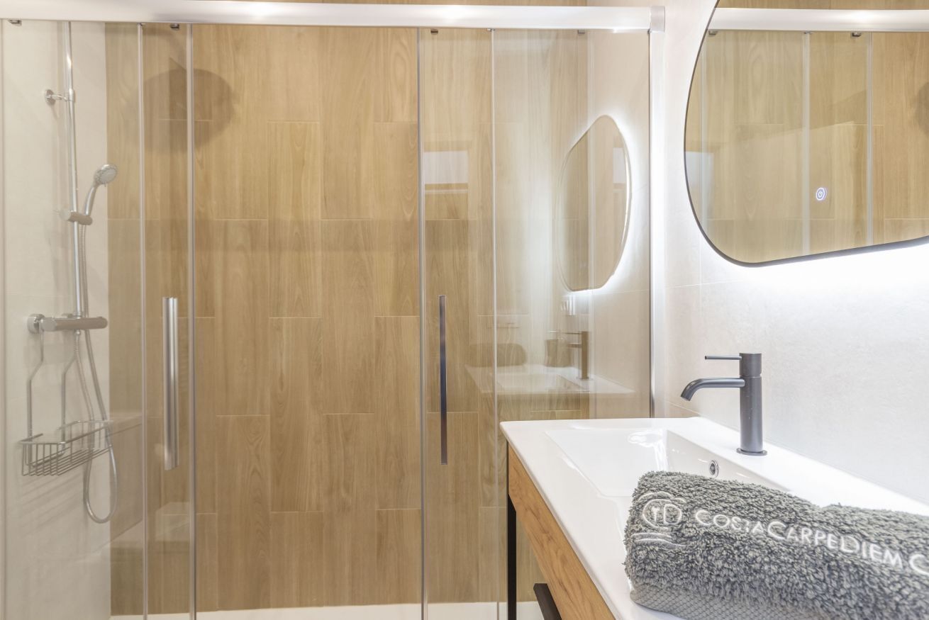 Une salle de bain moderne avec une douche à parois de verre, un plancher en bois, un lavabo blanc et une serviette posée sur le comptoir.