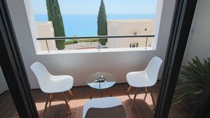 A balcony with two white chairs and a small table, overlooking a coastal view with cypress trees and a building. - Apartamento Anfiteatro by Costa CarpeDiem (Calpe)