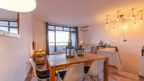 A modern dining area with a wooden table, white chairs, and a chandelier. - Apartamento Anfiteatro by Costa CarpeDiem (Calpe)