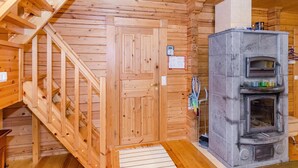 A wooden cabin interior with a stone fireplace, wooden staircase, and a door with a small sign.