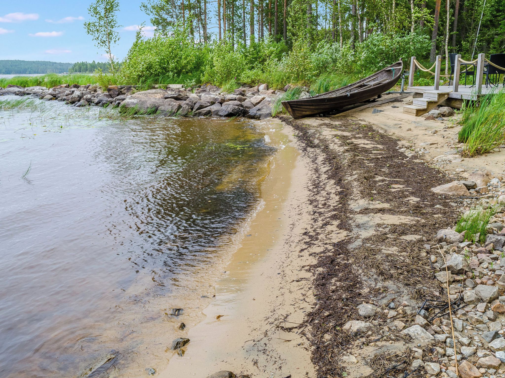 Ein ruhiger Fluss mit einem Holzboot, das an der Rechten Seite festgemacht ist, umgeben von felsigem Ufer und viel Grün.