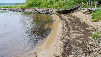 Ein ruhiger Fluss mit einem Holzboot, das an der Rechten Seite festgemacht ist, umgeben von felsigem Ufer und viel Grün.