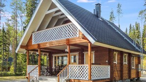A wooden cabin with a covered porch, a chimney, and a view of the surrounding forest.
