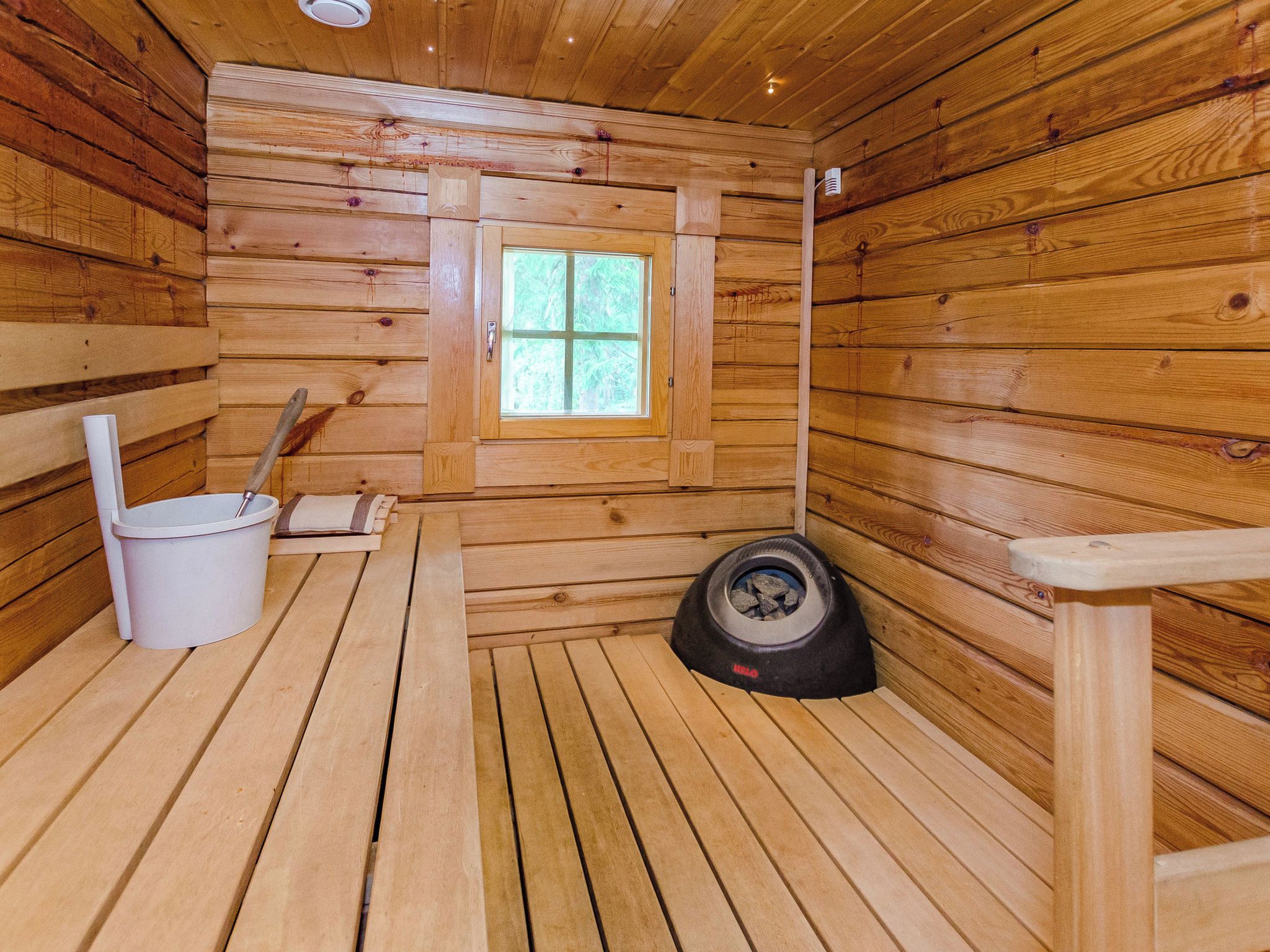 A wooden cabin interior with a window, a bucket, a shovel, and a sauna.