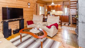 A cozy cabin interior with a living room, a TV, a fireplace, and a kitchen area.