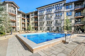 En flereetagers boligbygning med swimmingpool, altaner og udendørs siddepladser.