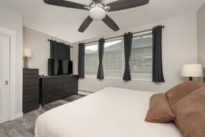 A bedroom with a bed, a dresser, a ceiling fan, and windows with curtains.