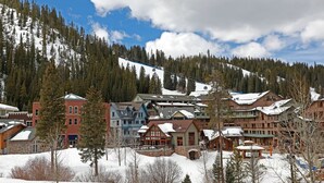 Une ville enneigée, avec un télésiège, des bâtiments en bois et une chaîne de montagnes en arrière-plan.