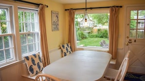 Un área de comedor con una mesa, sillas, una ventana con cortinas y vistas al jardín.