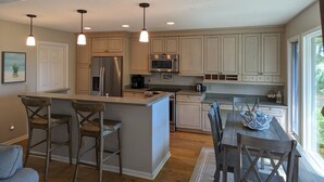 A modern kitchen with a central island, bar stools, a dining table with chairs, and a large window providing natural light. - 3 Bdrm 2 Bath Waterfront Villa on Dataw with Dock, Bikes, Pool and Beach Pass!  (St Helena Island)