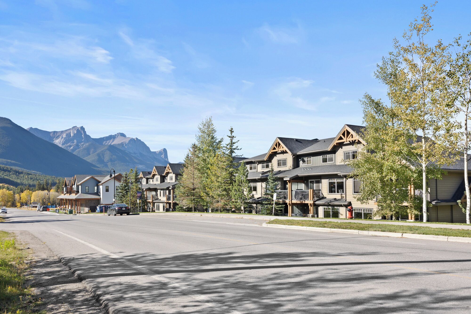 Eine Wohnstraße mit Häusern, blauem Himmel und Bergen im Hintergrund.