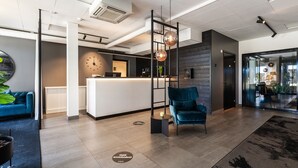 A modern hotel lobby with a reception desk, a blue sofa, a large plant, and a wooden wall.