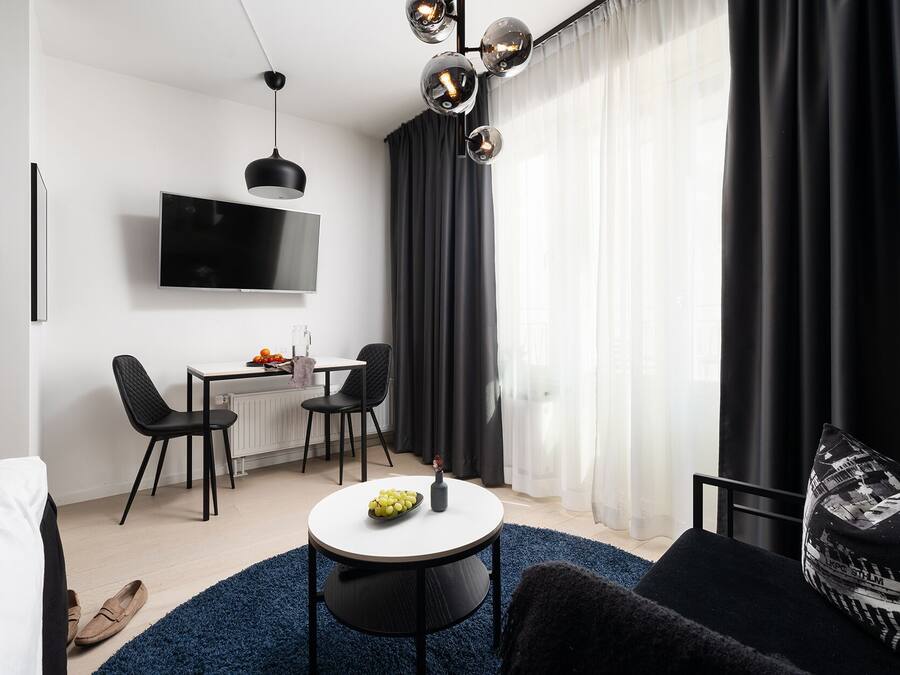 Una sala de estar moderna con un televisor de pantalla plana, una zona de comedor con dos sillas, una mesa redonda de centro y un sofá negro.