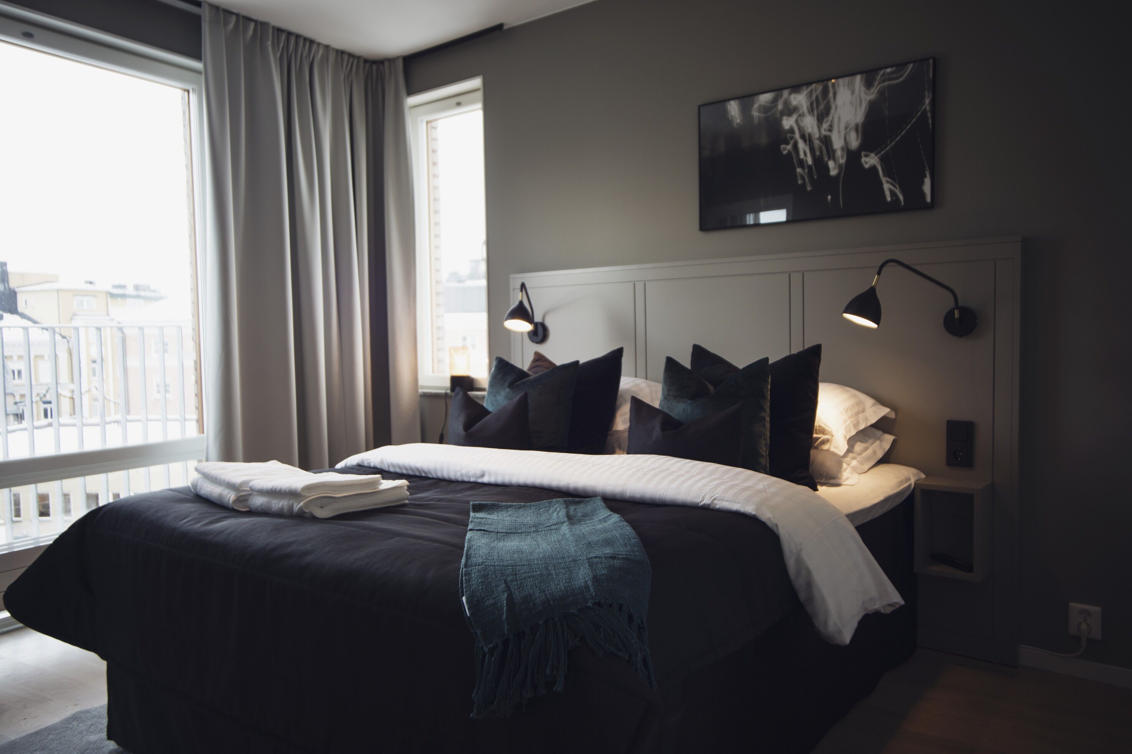 Habitación de hotel moderna con una cama grande, vistas a la ciudad y una obra de arte colgada sobre la cama.