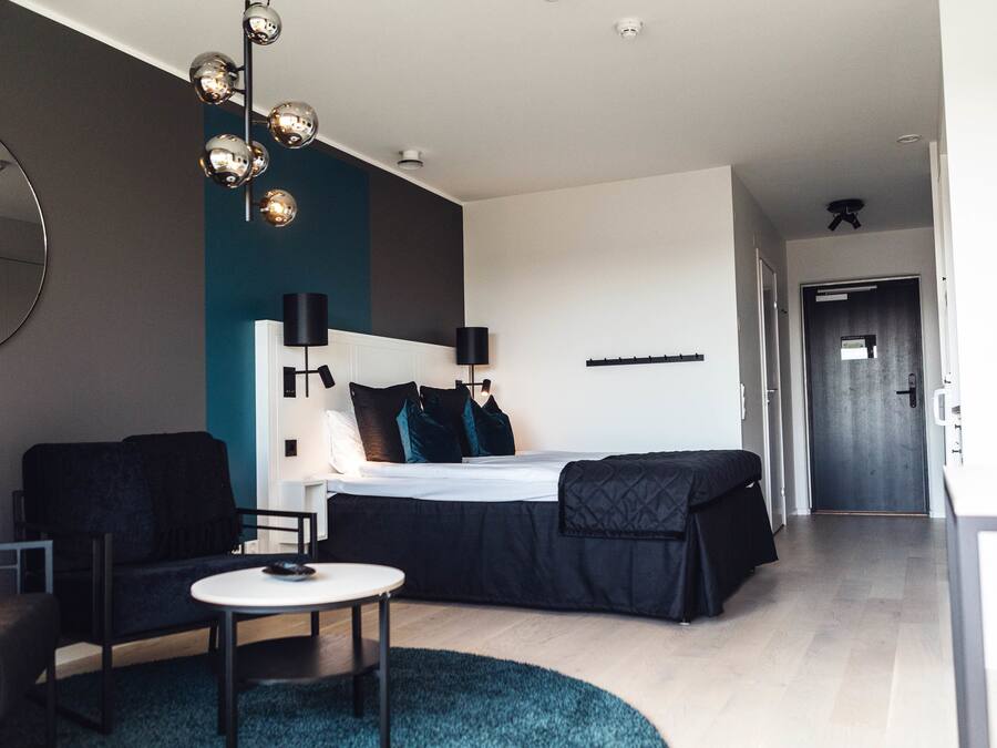 A modern hotel room with a bed, a sofa, a small table, and a round rug.