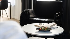 A modern room with a round white table, a black sofa, and a black chair. There's a book and a plate with food on the table.