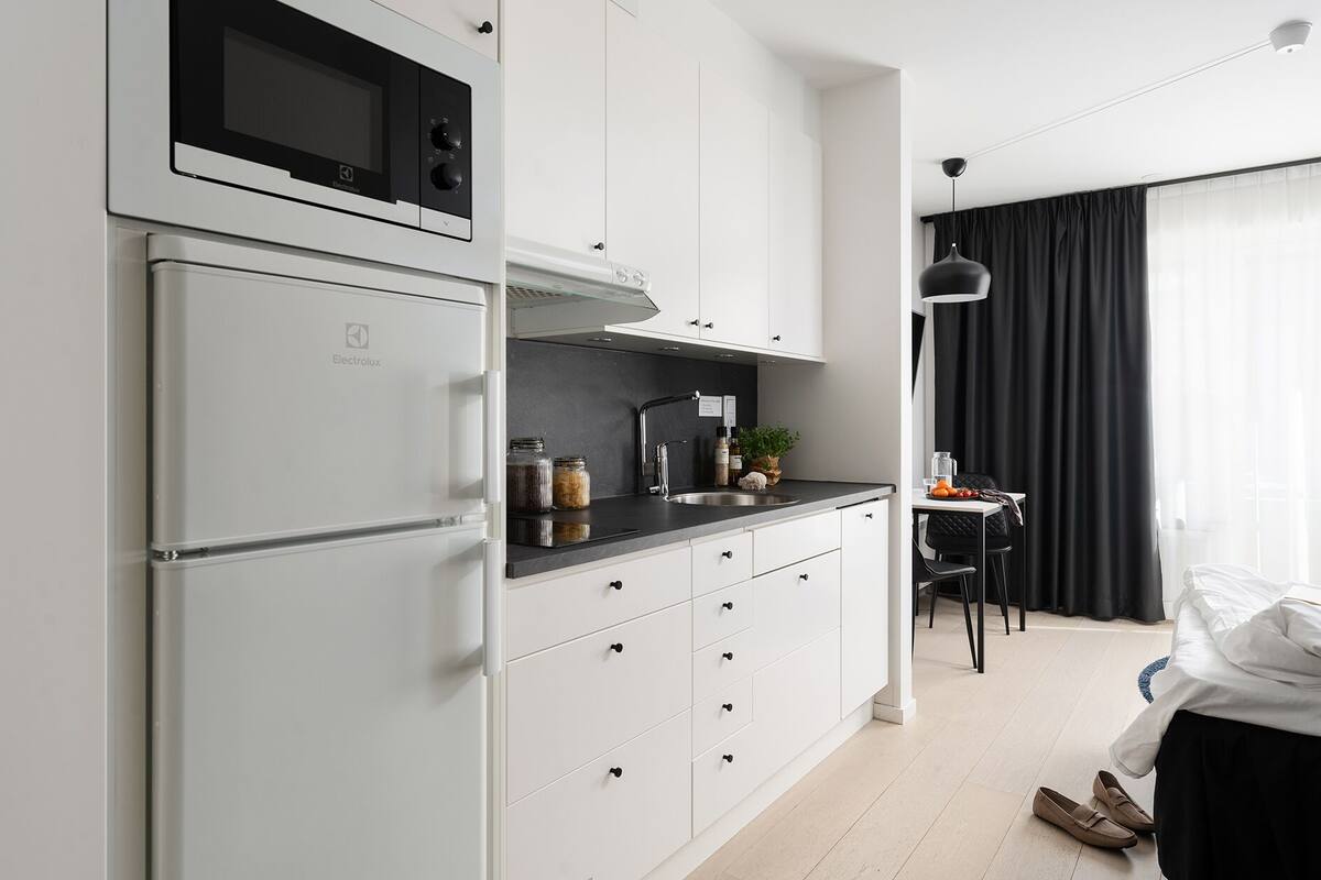Une cuisine moderne avec des meubles blancs, un four à micro-ondes encastré et un évier en acier inoxydable.