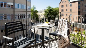 A balcony with two chairs and a small round table, featuring a book and a bowl of fruit.