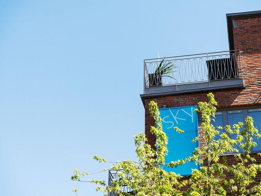 Un edificio con un letrero azul, un balcón con barandillas de metal y un árbol en primer plano.