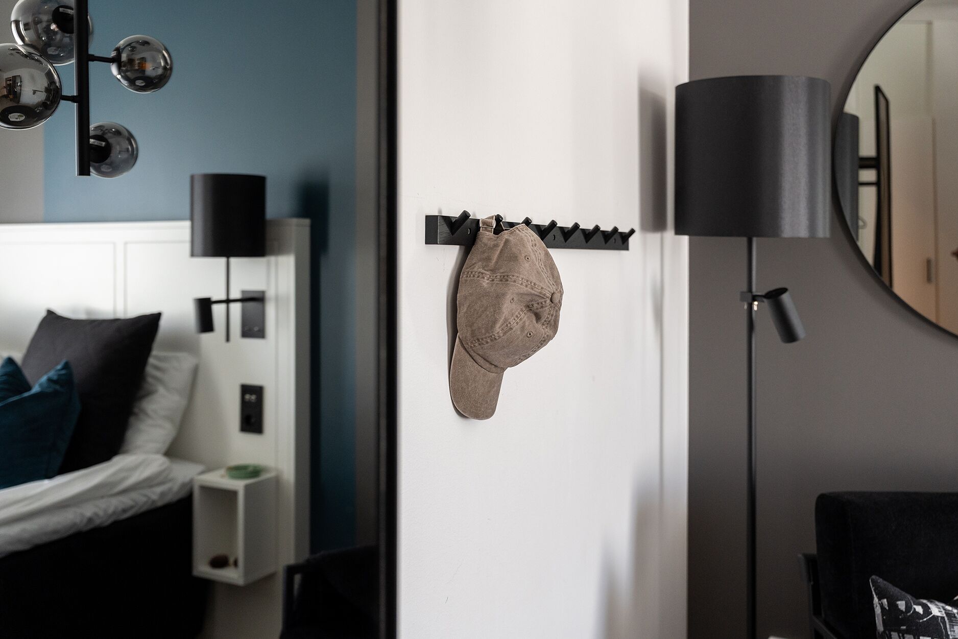 Un dormitorio con cama, un perchero de pared, una lámpara de pie y un espejo.