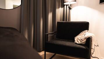 A hotel room with a bed, a chair, a lamp, and a window with curtains.
