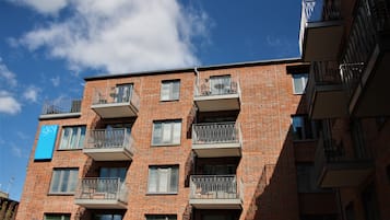 Un edificio de ladrillo de varios pisos con balcones, un letrero azul y un cielo despejado.