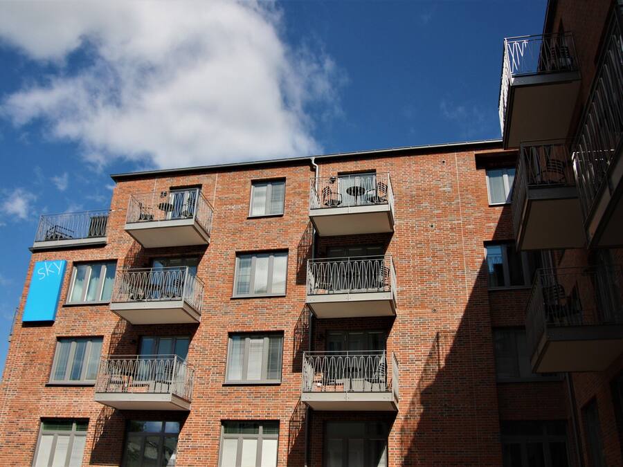 Un edificio de ladrillo de varios pisos con balcones, un letrero azul y un cielo despejado.